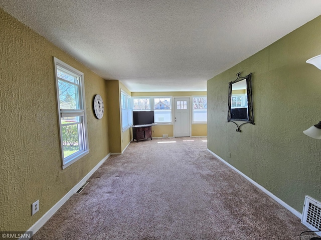 unfurnished living room with a textured ceiling, a textured wall, visible vents, and a healthy amount of sunlight