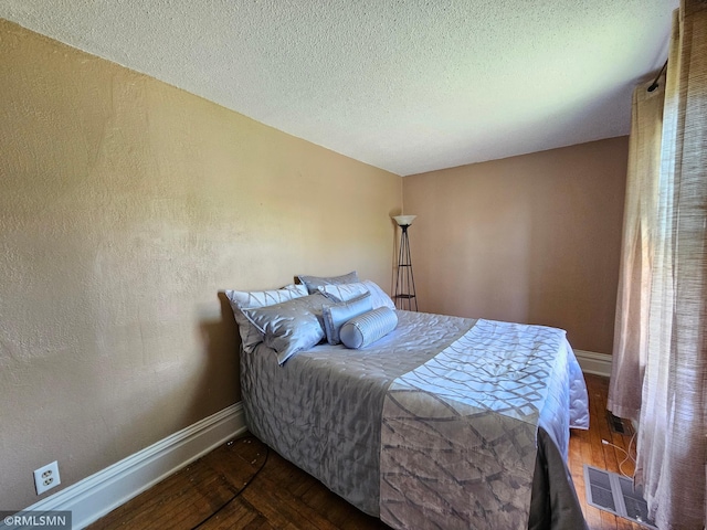 bedroom with visible vents, a textured ceiling, baseboards, and wood finished floors