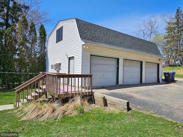 view of home's exterior featuring a detached garage, an AC wall unit, an outdoor structure, a gambrel roof, and a shingled roof