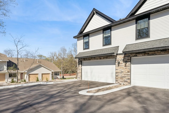 view of front facade with an attached garage, driveway, a shingled roof, and stone siding