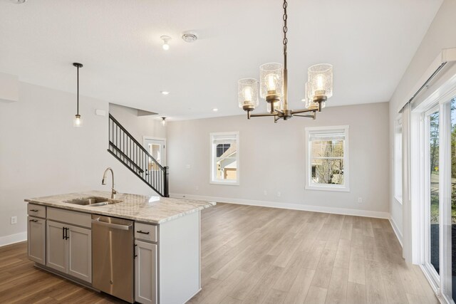 kitchen featuring stainless steel dishwasher, light wood-style floors, a chandelier, light stone counters, and a sink