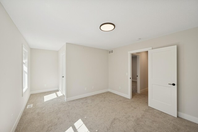 unfurnished bedroom with baseboards, light colored carpet, and visible vents
