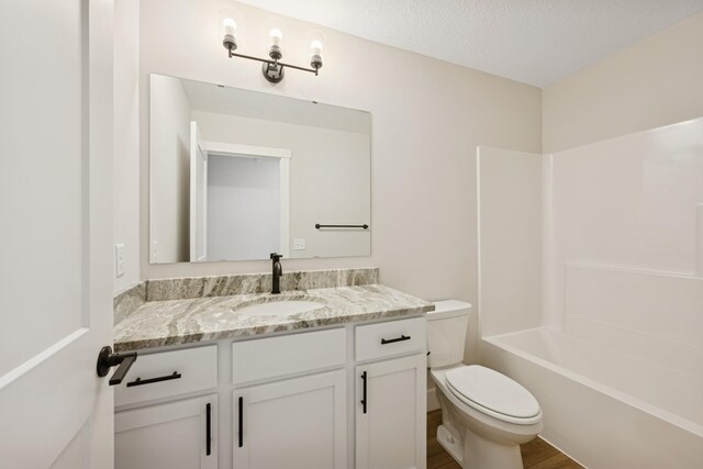 full bathroom featuring vanity, wood finished floors, toilet, washtub / shower combination, and a textured ceiling