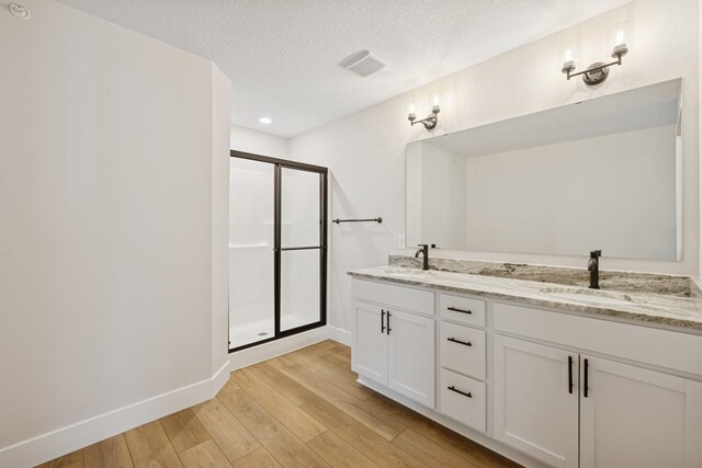 full bath with baseboards, a sink, wood finished floors, and a stall shower