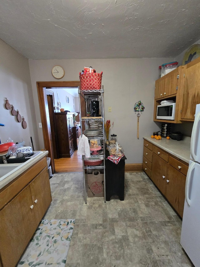 kitchen featuring white appliances, baseboards, light countertops, brown cabinets, and stone finish flooring