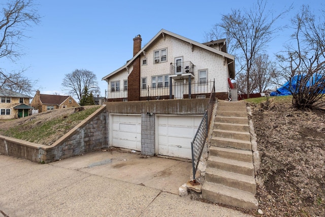 exterior space featuring an attached garage, stairway, a chimney, concrete driveway, and a balcony