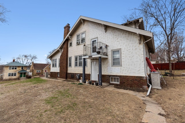 view of front facade with fence, a chimney, stucco siding, and a balcony