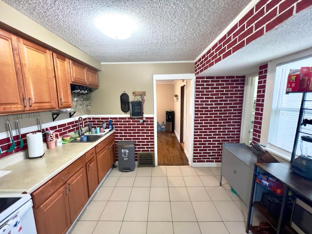 kitchen featuring a sink, light countertops, a textured ceiling, brick wall, and visible vents
