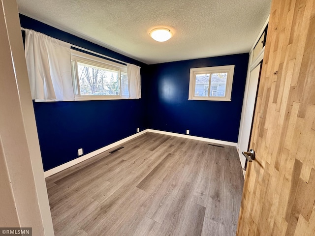 empty room featuring baseboards, plenty of natural light, a textured ceiling, and wood finished floors