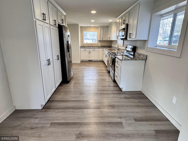 kitchen featuring appliances with stainless steel finishes, dark stone countertops, recessed lighting, and wood finished floors