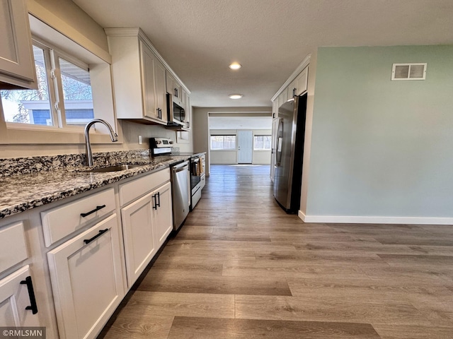 kitchen with appliances with stainless steel finishes, a sink, dark stone counters, recessed lighting, and light wood-type flooring