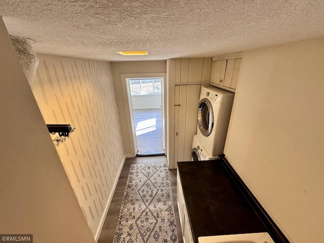 laundry room with baseboards, stacked washer and dryer, a textured ceiling, and cabinet space