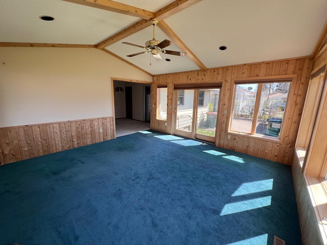 carpeted spare room with a wainscoted wall, vaulted ceiling with beams, wood walls, and ceiling fan