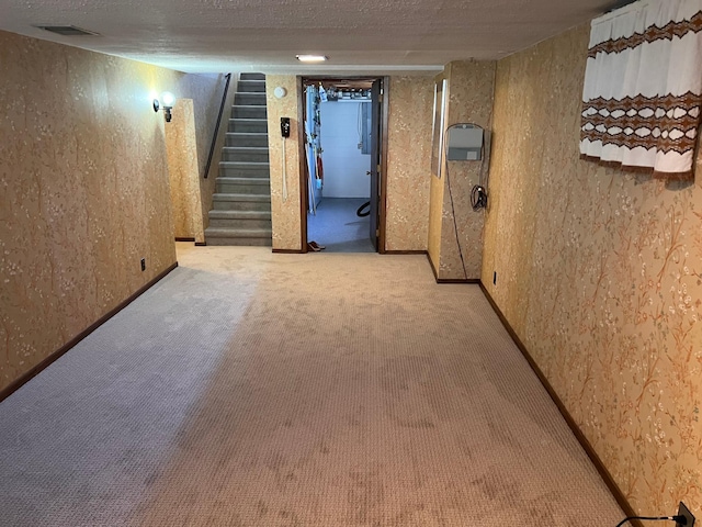 finished below grade area with visible vents, a textured wall, stairway, a textured ceiling, and carpet flooring