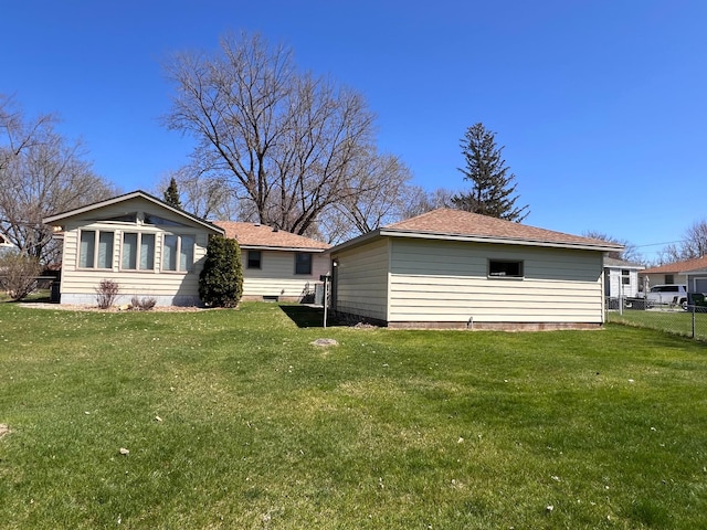 back of house with a lawn, fence, and roof with shingles