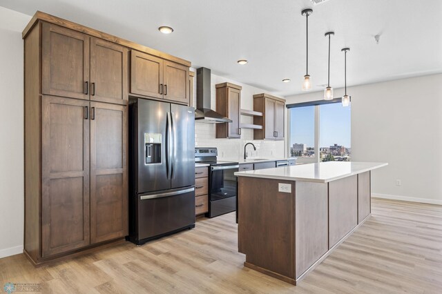 kitchen featuring baseboards, stainless steel appliances, light wood-type flooring, and wall chimney exhaust hood