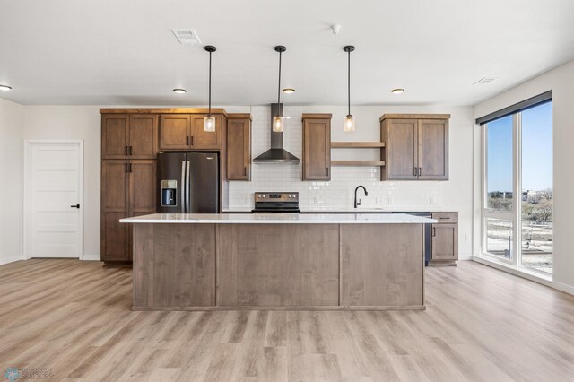 kitchen featuring light wood-type flooring, light countertops, wall chimney range hood, and stainless steel appliances