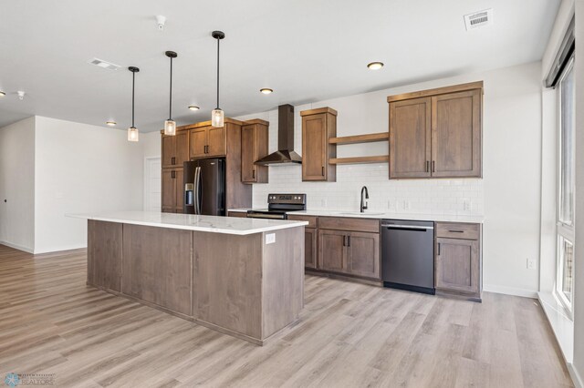 kitchen featuring visible vents, appliances with stainless steel finishes, light wood-type flooring, a sink, and wall chimney exhaust hood