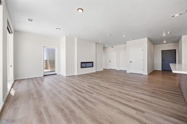 unfurnished living room with a glass covered fireplace, baseboards, light wood-style flooring, and visible vents