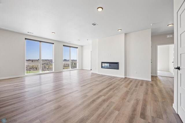 unfurnished living room featuring light wood-style floors, a glass covered fireplace, recessed lighting, baseboards, and visible vents