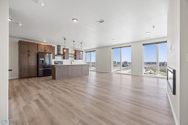 kitchen with light wood-style floors, wall chimney exhaust hood, open floor plan, refrigerator with ice dispenser, and visible vents