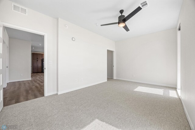 carpeted spare room with visible vents, baseboards, and ceiling fan