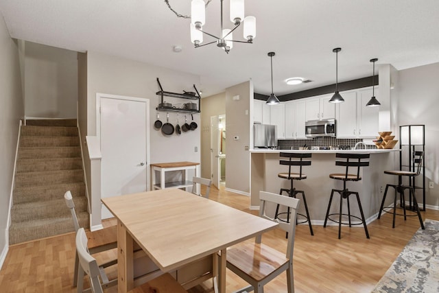 dining room with baseboards, light wood-style flooring, stairway, and an inviting chandelier