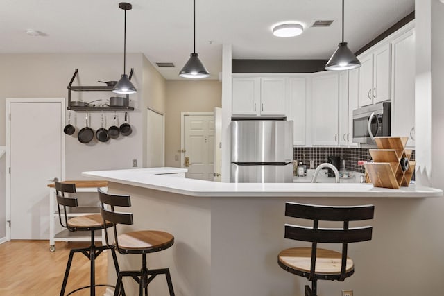 kitchen featuring backsplash, visible vents, a peninsula, stainless steel appliances, and white cabinetry