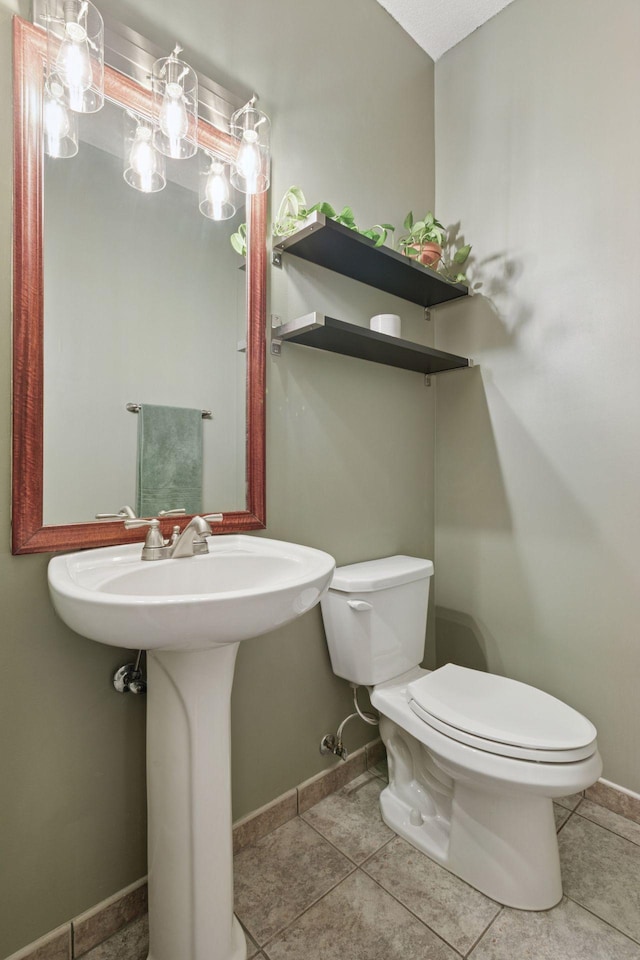 bathroom with toilet, baseboards, and tile patterned flooring
