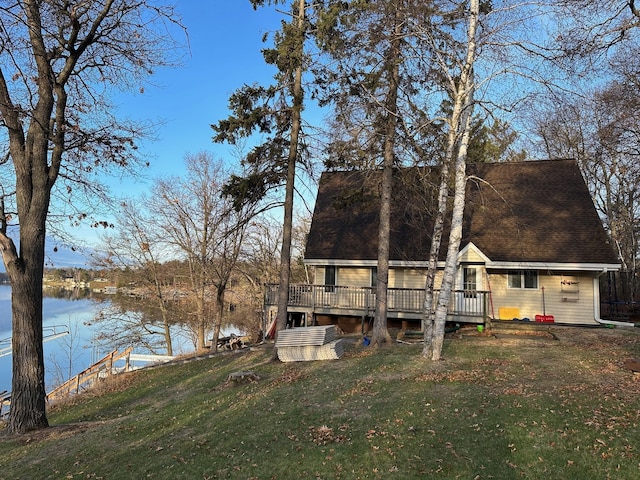 rear view of house featuring a lawn, roof with shingles, and a deck with water view