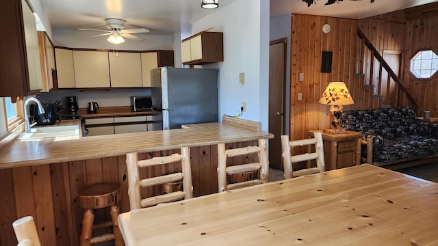 kitchen featuring a sink, wood walls, a ceiling fan, stainless steel microwave, and a peninsula