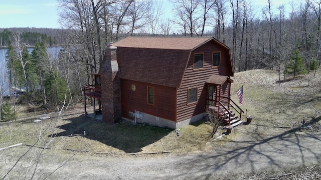 view of side of property featuring a shingled roof, a view of trees, and a gambrel roof