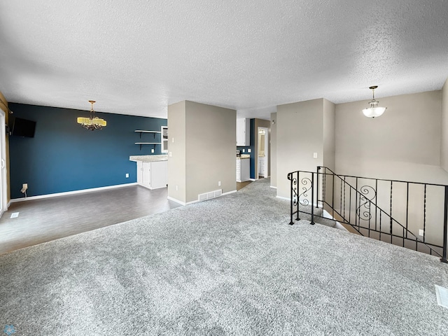 carpeted empty room featuring visible vents, a textured ceiling, baseboards, and an inviting chandelier