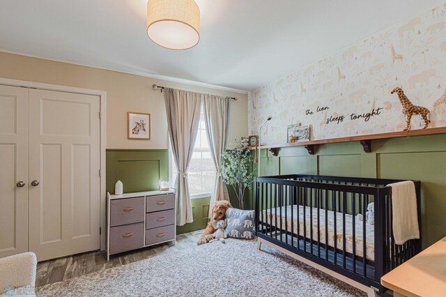 bedroom with ornamental molding, wood finished floors, a decorative wall, a wainscoted wall, and a nursery area