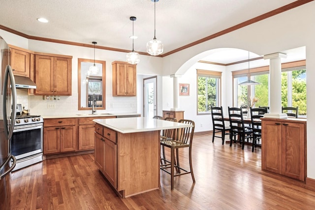 kitchen featuring brown cabinets, a breakfast bar, a sink, stainless steel range with gas stovetop, and arched walkways