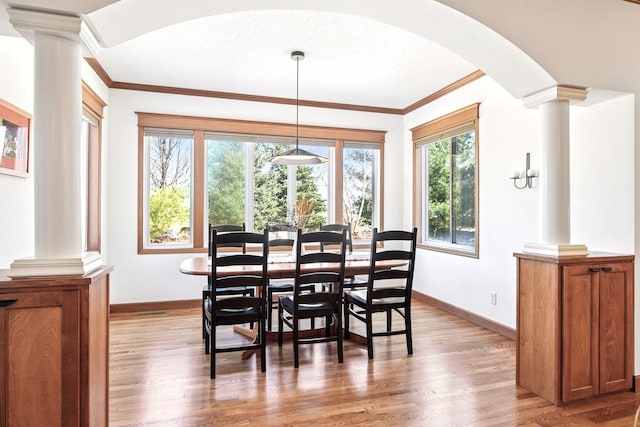 dining area featuring decorative columns, arched walkways, wood finished floors, baseboards, and ornamental molding