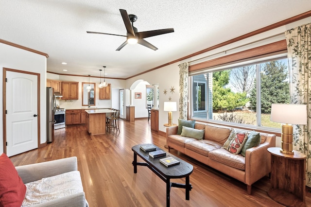 living area with crown molding, wood finished floors, ceiling fan, a textured ceiling, and arched walkways
