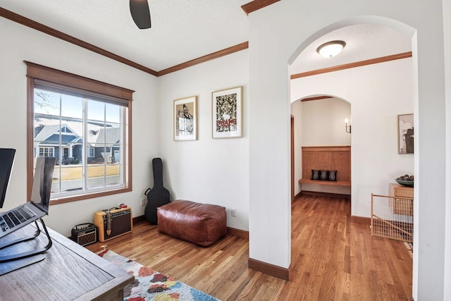 office with arched walkways, ceiling fan, ornamental molding, and light wood-style floors
