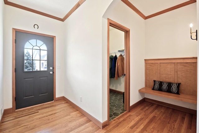 foyer entrance with crown molding, arched walkways, light wood finished floors, and baseboards