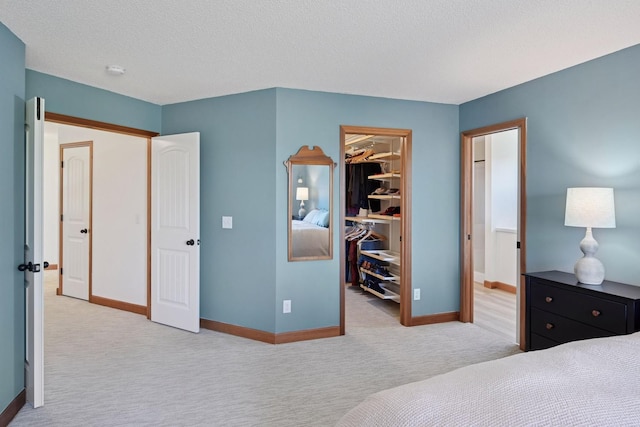 carpeted bedroom with a closet, baseboards, ensuite bathroom, a walk in closet, and a textured ceiling