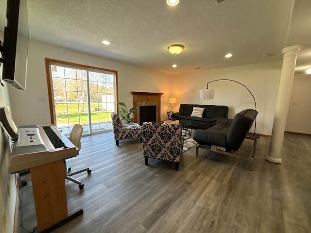 living area featuring a fireplace, a textured ceiling, recessed lighting, decorative columns, and wood finished floors