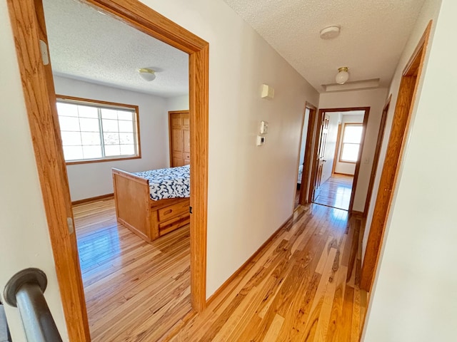 hallway with light wood-style floors, baseboards, plenty of natural light, and a textured ceiling