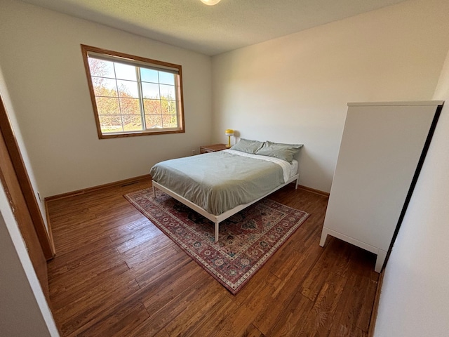 bedroom featuring baseboards, a textured ceiling, and wood finished floors