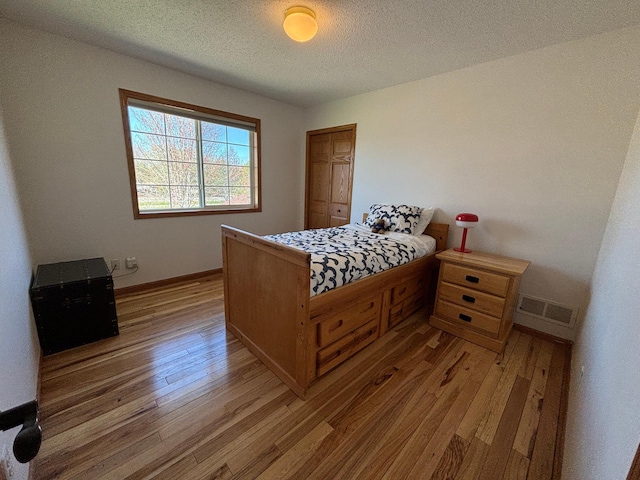 bedroom with a textured ceiling, baseboards, visible vents, and light wood-type flooring