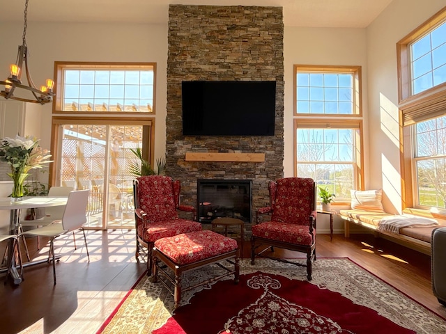 living area featuring a towering ceiling, a stone fireplace, and wood finished floors