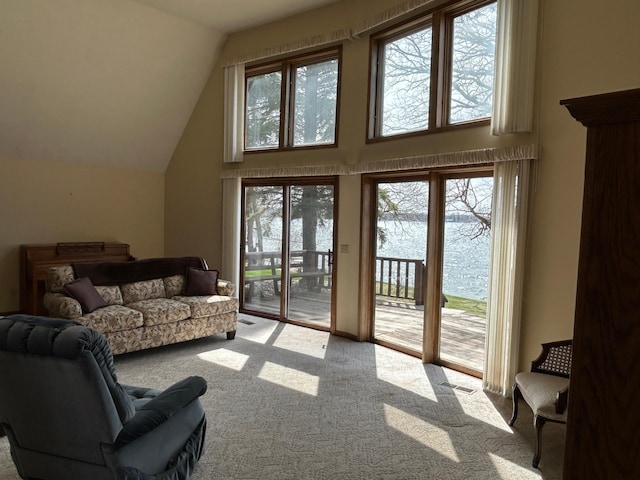 living area with high vaulted ceiling, visible vents, a wealth of natural light, and carpet