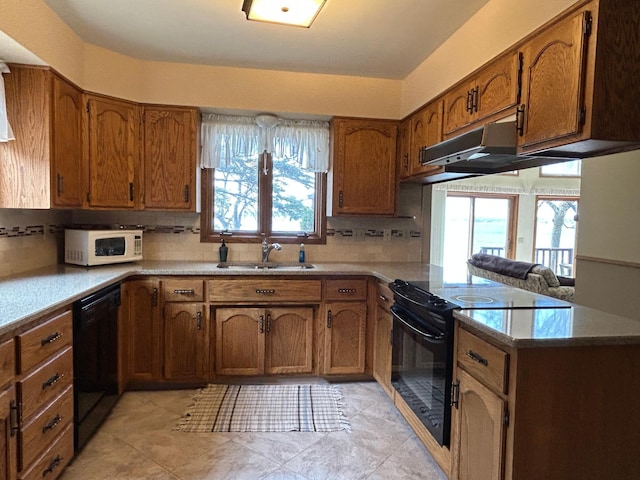 kitchen with a peninsula, brown cabinets, a sink, backsplash, and black appliances