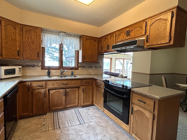 kitchen featuring decorative backsplash, under cabinet range hood, brown cabinets, a sink, and black appliances