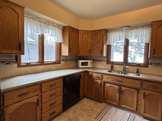 kitchen with tasteful backsplash, brown cabinets, a sink, white microwave, and black dishwasher