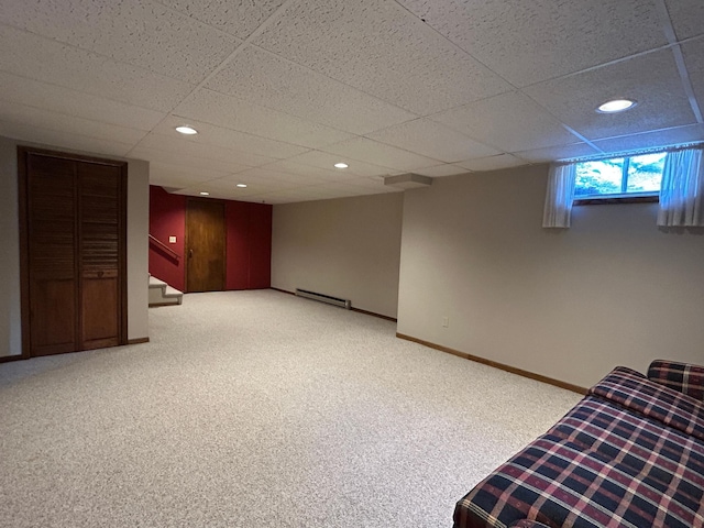 below grade area featuring stairs, baseboards, light colored carpet, a paneled ceiling, and a baseboard heating unit